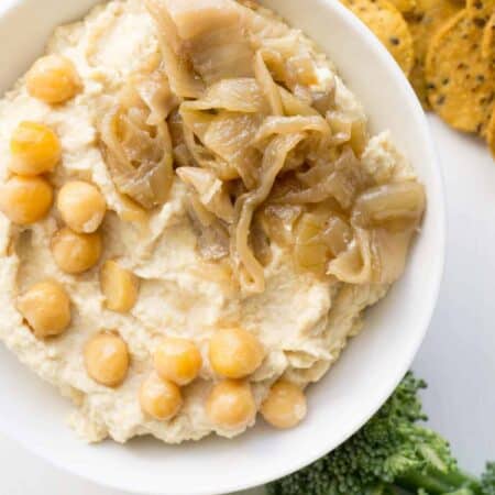 bowl of caramelized onion hummus with crackers and broccoli for dipping.