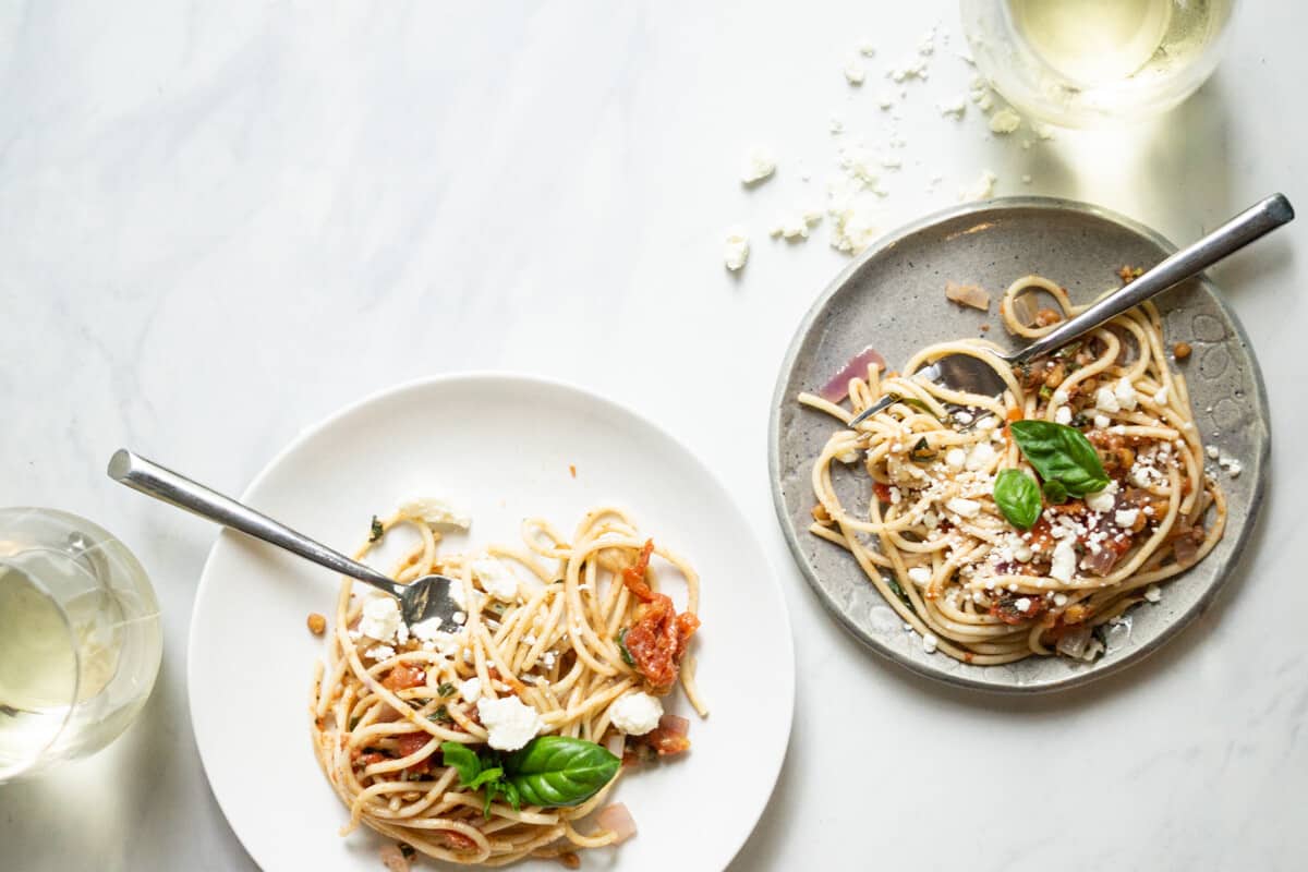 two plates of summer spaghetti with glasses of white wine