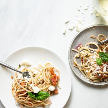 two plates of summer spaghetti with glasses of white wine