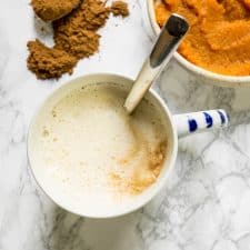 A mug of homemade pumpkin spice latte with a spoonful of spices and a bowl of pumpkin puree.