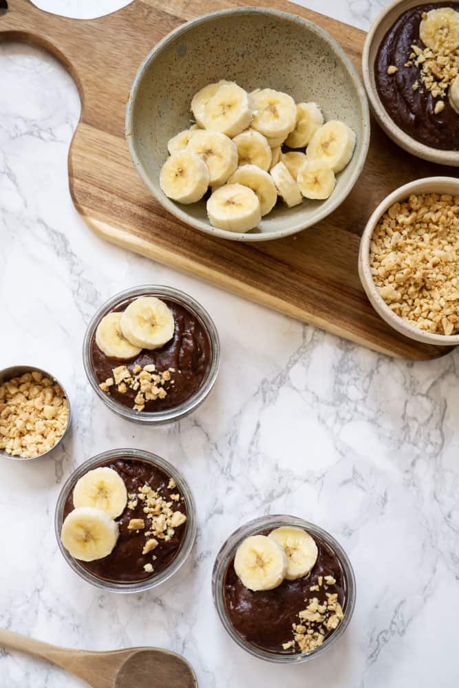 3 bowls of Chocolate Pudding with Peanut Butter topped with bananas and chopped peanuts