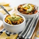 two bowls of turkey quinoa chili surrounded by tortilla chips and half an avocado in the background