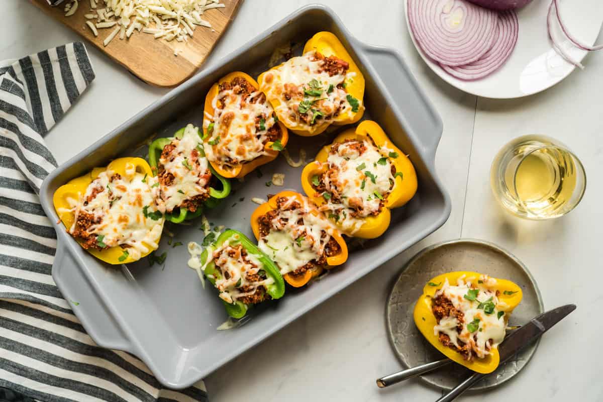 a baking pan with quinoa stuffed pizza peppers along side a glass of wine and one pepper on a plate