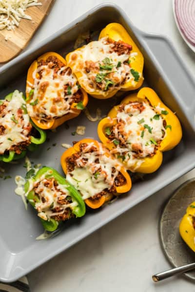 a baking pan with quinoa stuffed pizza peppers along side a glass of wine and one pepper on a plate