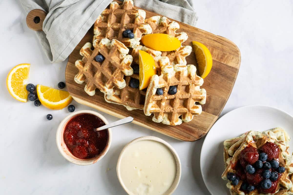 platter of orange poppyseed protein waffles with two sauce options : berry and vanilla custard