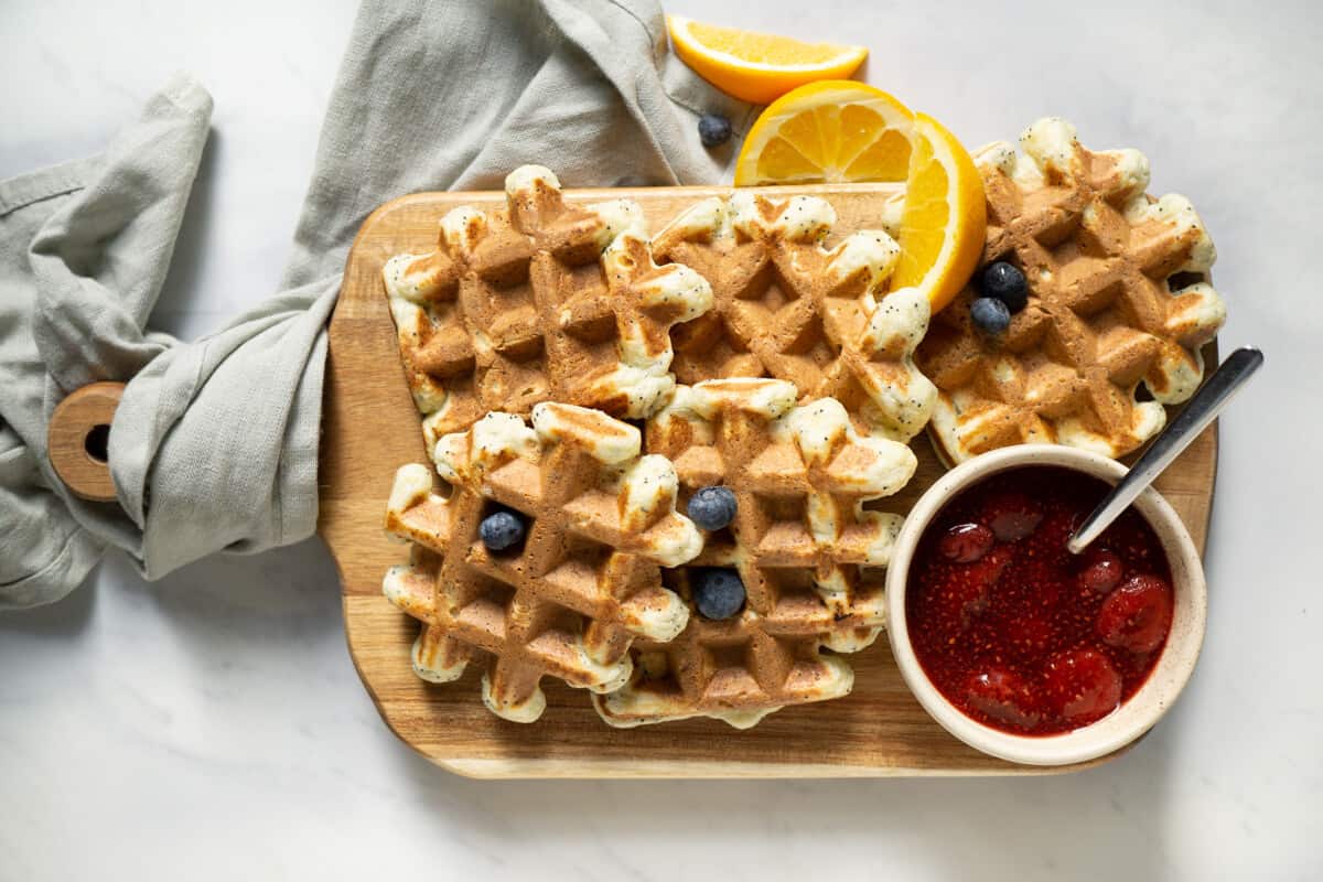platter of orange poppyseed protein waffles with a bowl of strawberry sauce