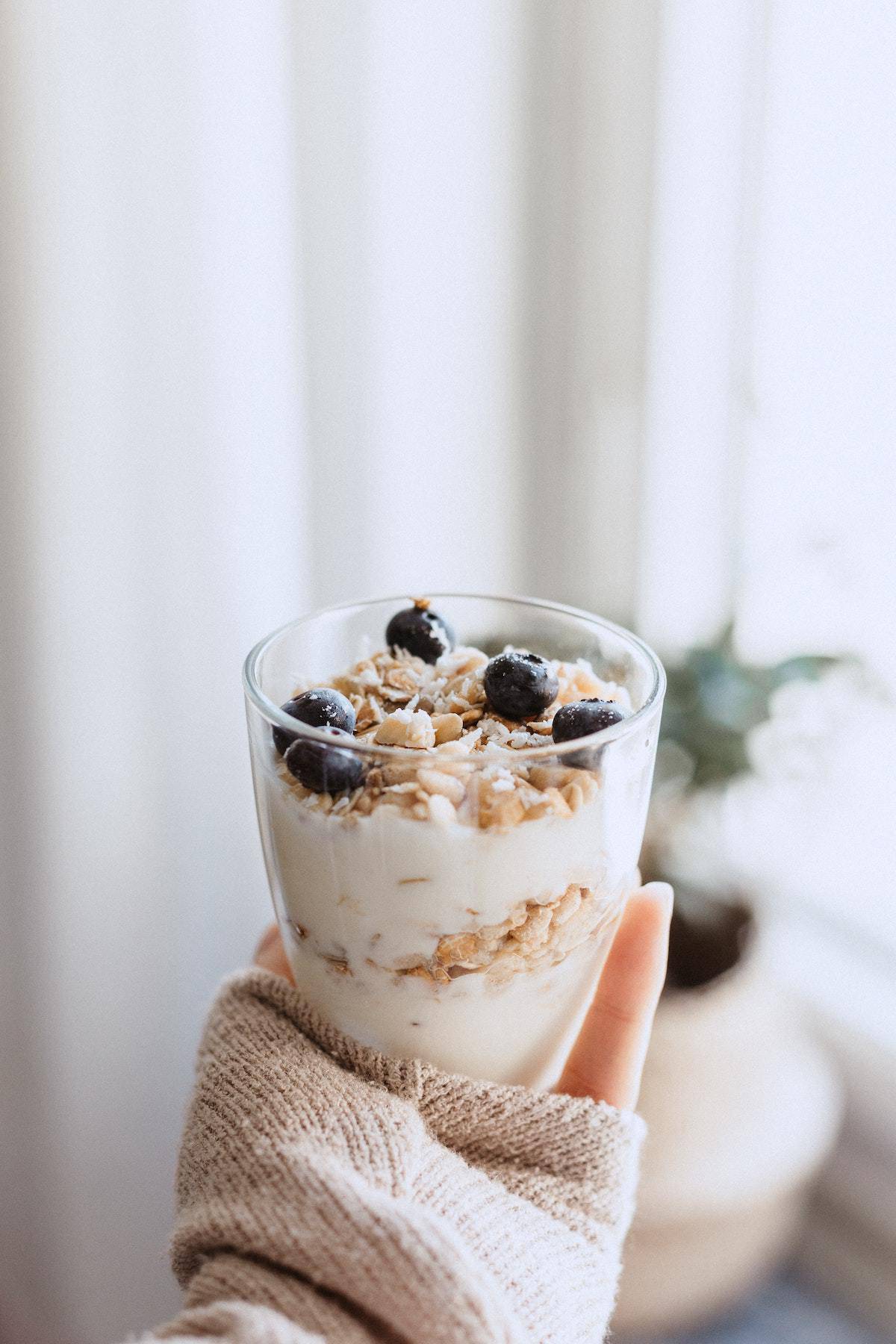 arm outstretched holding a yogurt and blueberry parfait in front of a window