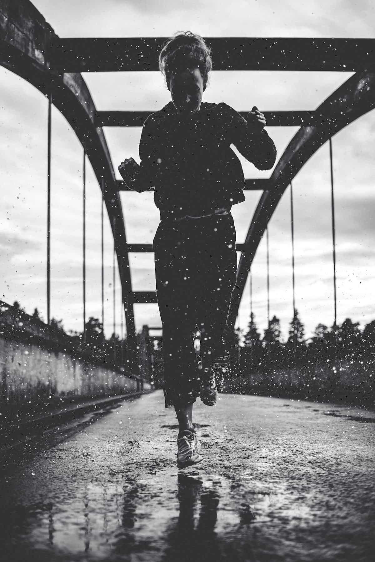 black-and-white-photo-of-woman-running-on-bridge-in-the-rain