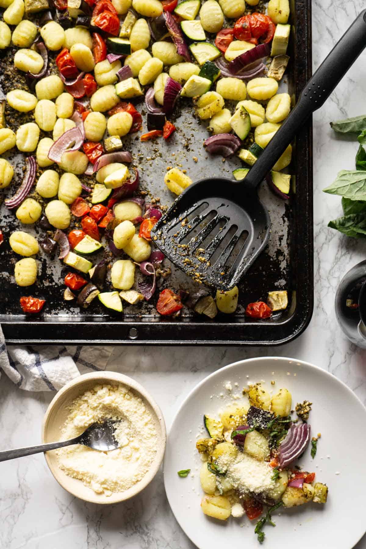 Overview of pesto gnocchi on a sheetpan and served on a plate with a glass of wine and parmesan cheese