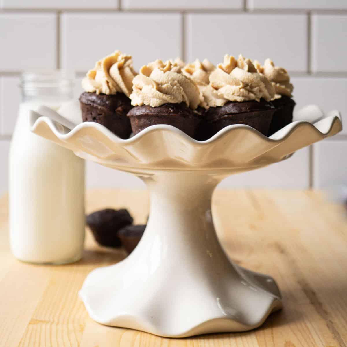 A raised cake stand with frosted two bite protein brownies and a jar of milk