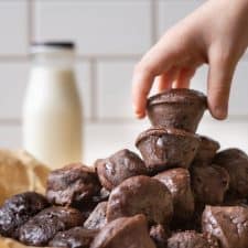 A pile of two bite protein brownies with a hand reaching for the top brownie and a bottle of milk in the background