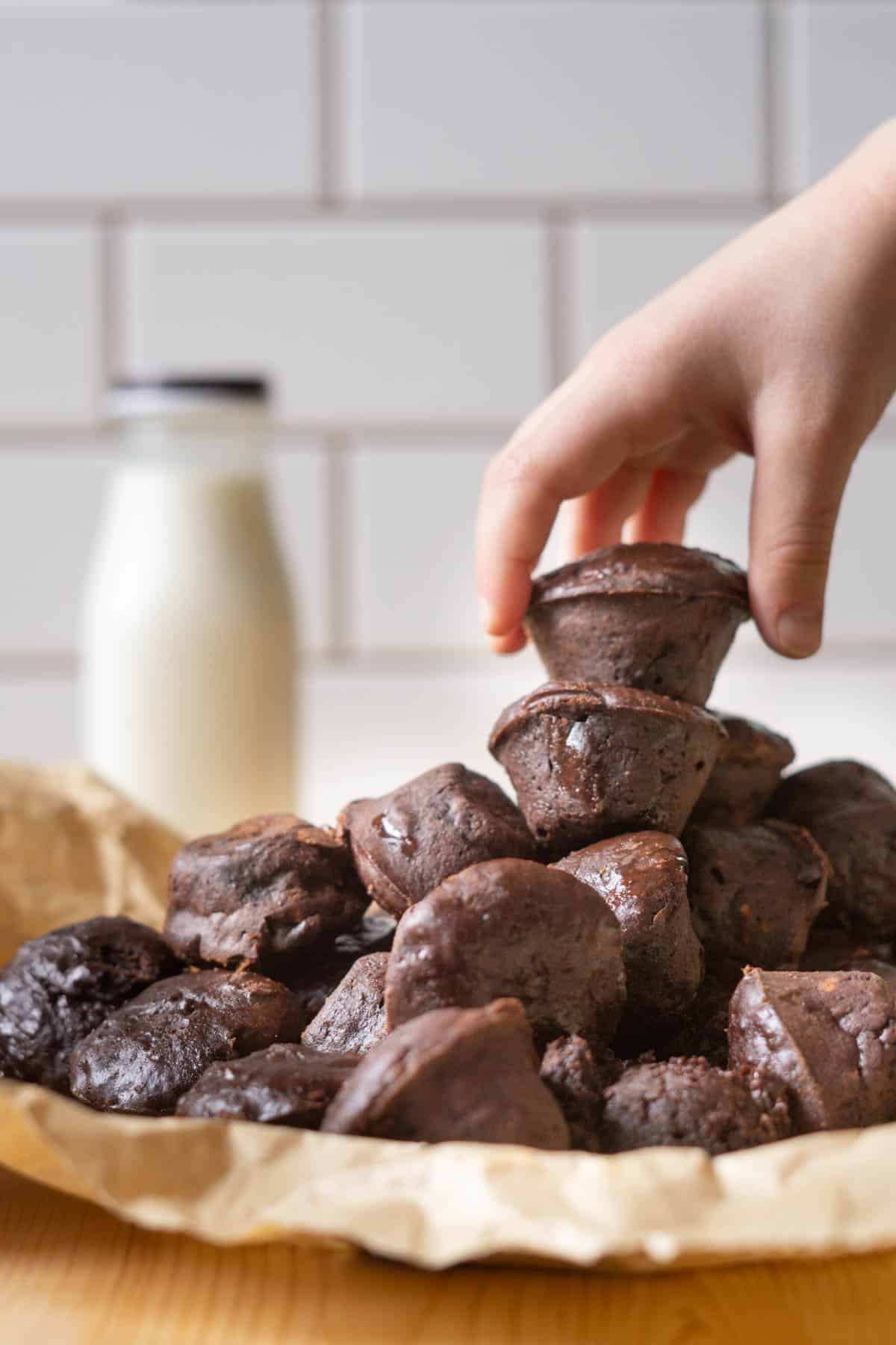 A pile of two bite protein brownies with a hand reaching for the top brownie and a bottle of milk in the background