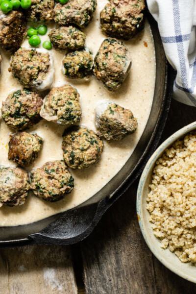 Swedish meatballs in sauce in pan beside a bowl of brown rice