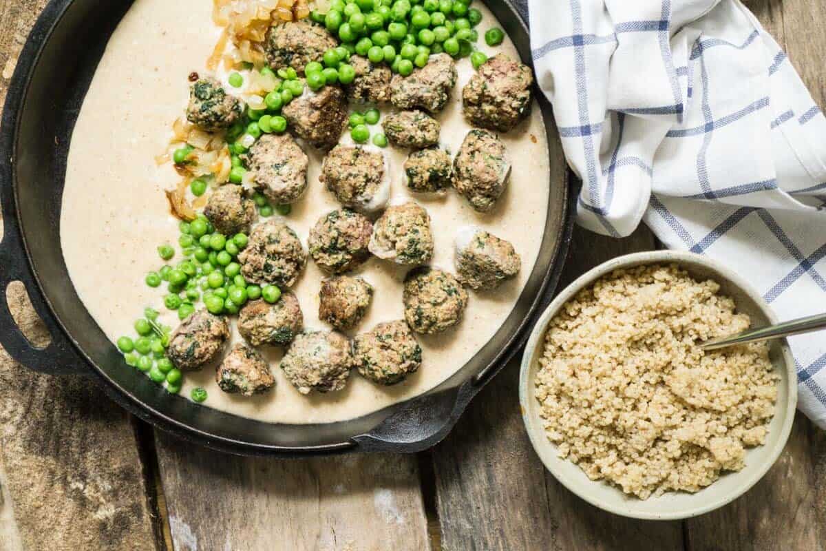 swedish meatballs in a cast iron pan with a bowl of rice and peas