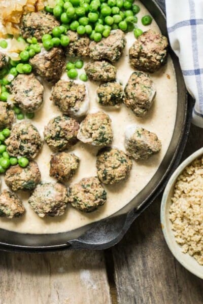 swedish meatballs in a cast iron pan with a bowl of rice and peas