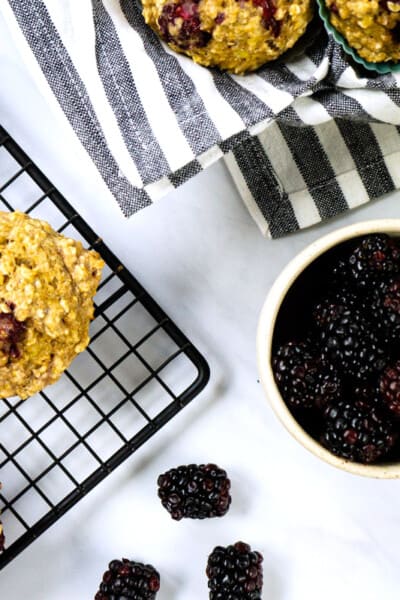 overhead view of blackberry oatmeal muffins cooling on a rack beside a bowl of fresh blackberries and two glass jars of milk