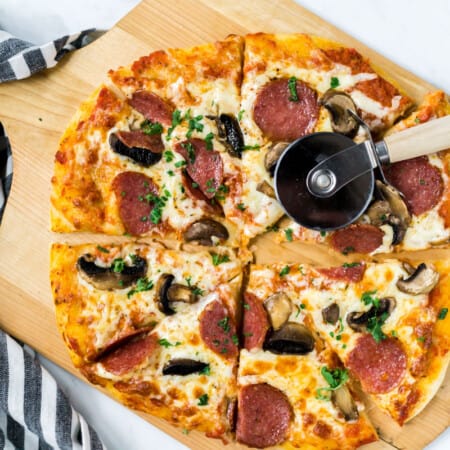 a baked and sliced sourdough pizza topped with salami and mushrooms lying on a pizza peel with a pizza slicer