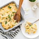 Baking dish with creamy tuna noodle casserole with a serving spoon that has scooped out a plateful, which is right beside the baking dish.
