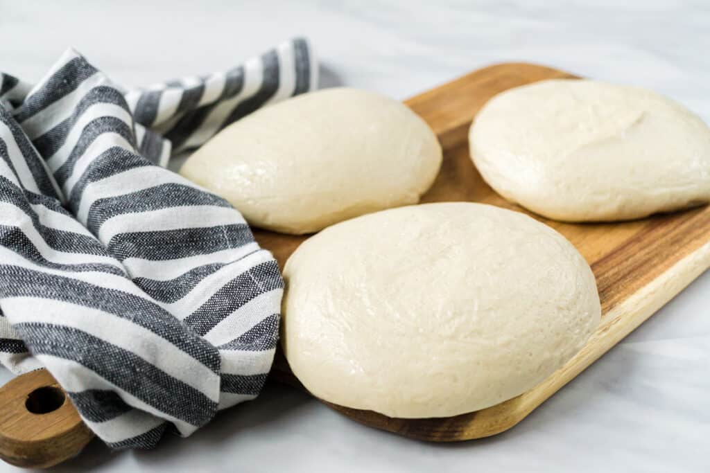 Three balls of sourdough pizza dough on a wooden cutting board. 