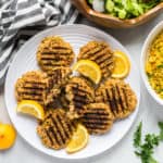 A plate of pistachio salmon cakes with a salad and a bowl of apricot rice to the side.