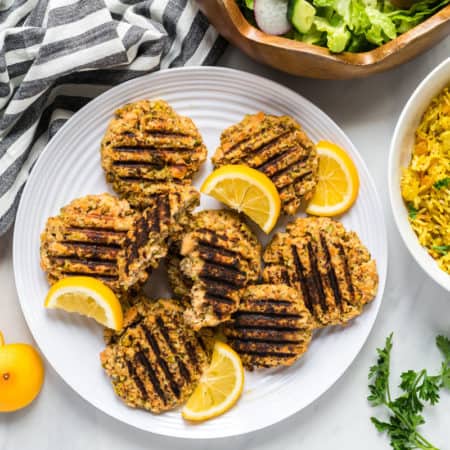 A plate of pistachio salmon cakes with a salad and a bowl of apricot rice to the side.