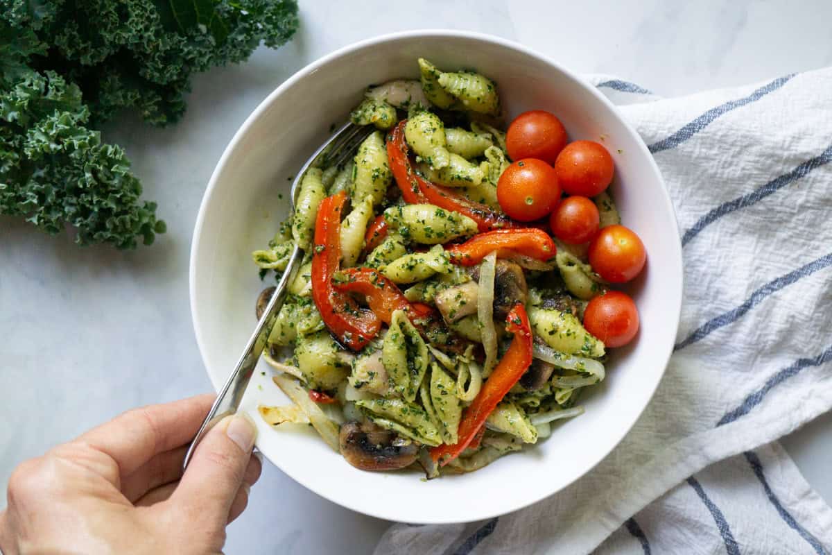 A bowl of penne dressed with a vegan walnut pesto and topped with veggies.