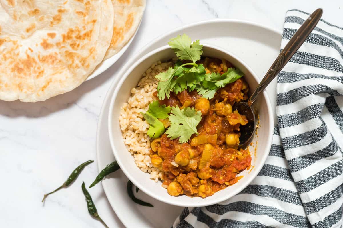 a bowl of chana masala with brown rice with some green chilis and paratha