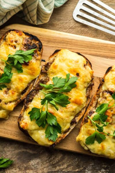 A serving board with three French Onion Beef open face sandwiches. These are topped with melted Emmentaler cheese.