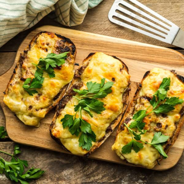 A serving board with three French Onion Beef open face sandwiches. These are topped with melted Emmentaler cheese.